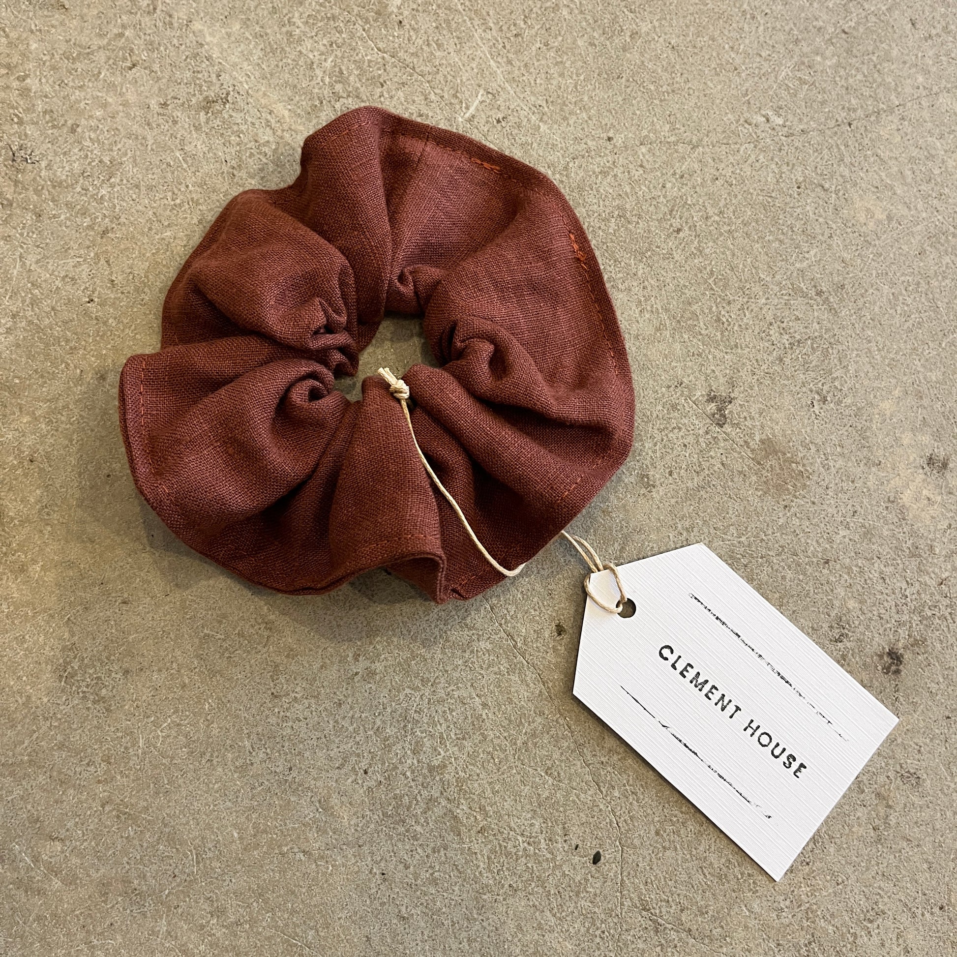 Brown scrunchie with a tag labeled 'Clement House' on a textured surface
