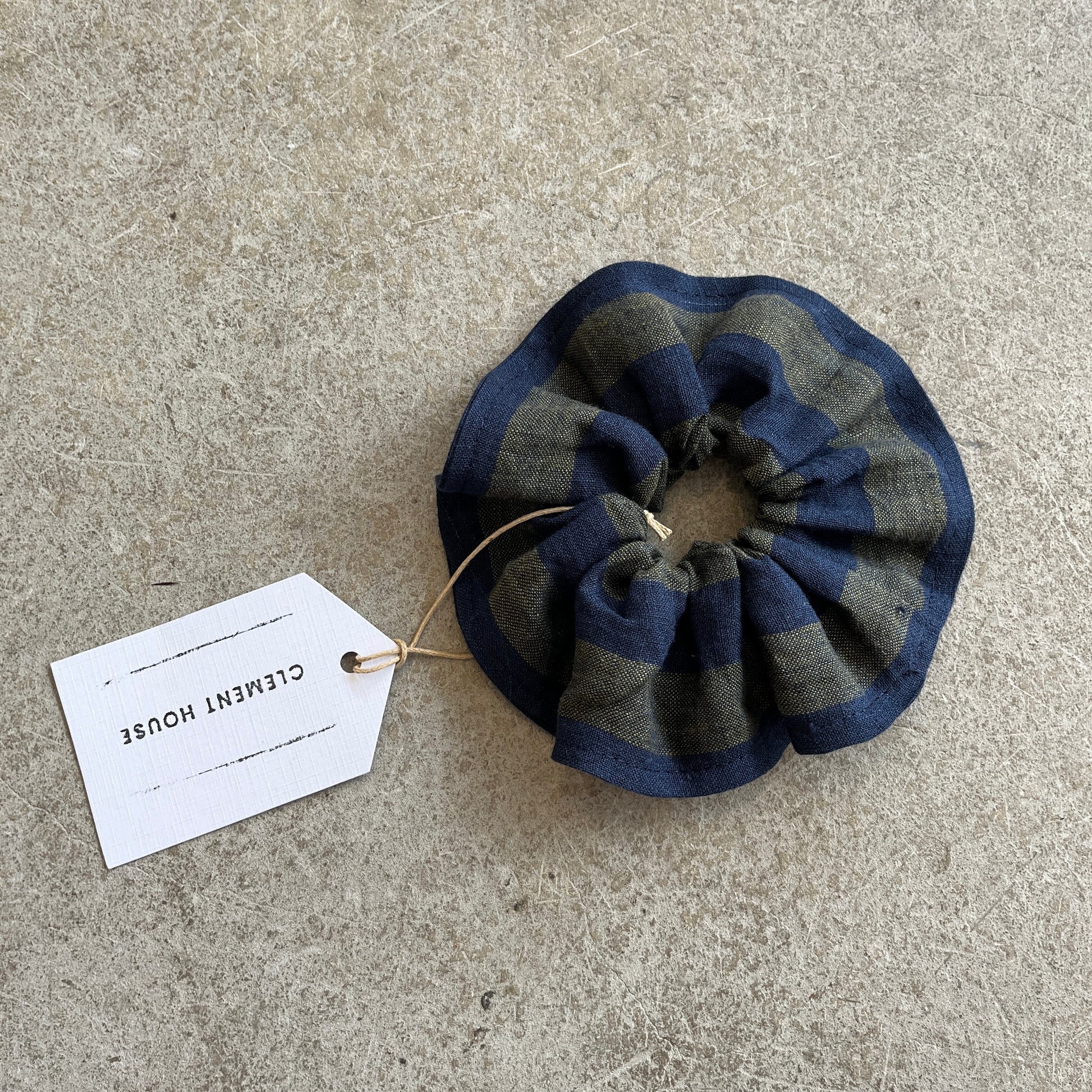 Blue and green striped scrunchie with a label on a concrete surface