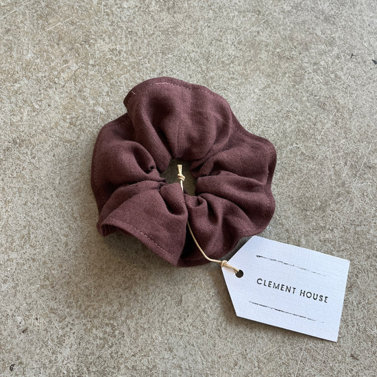 Brown scrunchie with a tag labeled 'Clement House' on a concrete surface