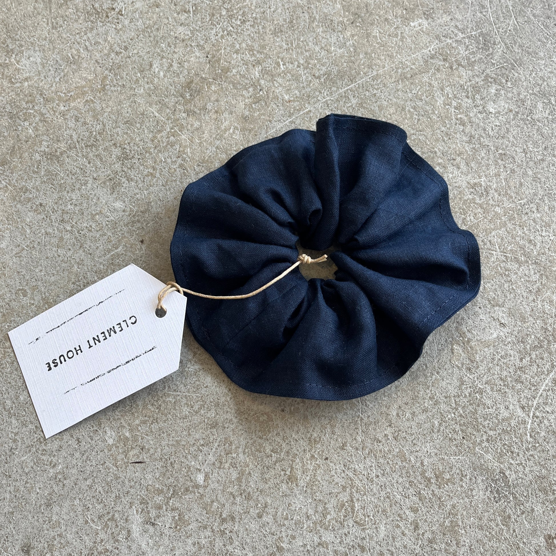 Navy blue scrunchie with a tag on a gray surface
