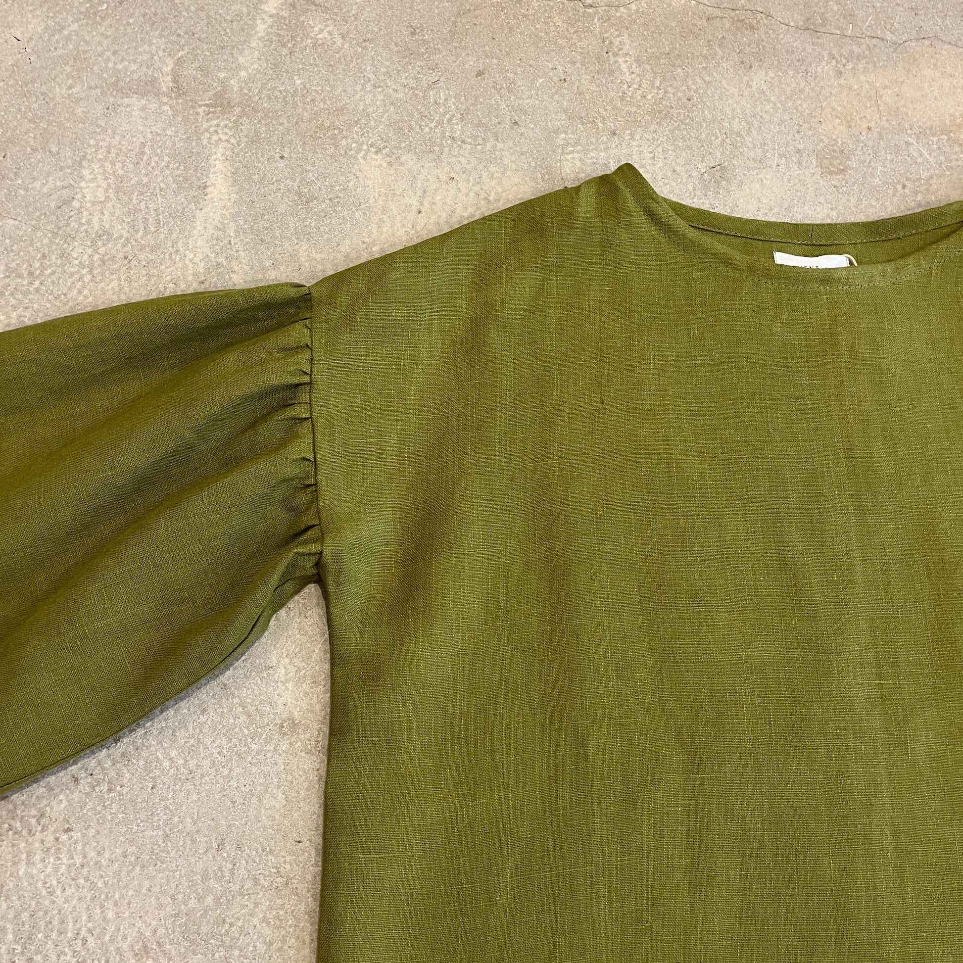Green long-sleeve top on a textured beige surface