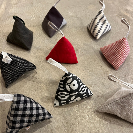 Triangular lavender fabric pouches in various patterns and colours with loop hangers on a concrete surface