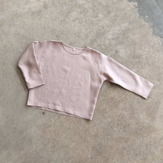 A pink, long-sleeved crop top laid flat on a concrete surface.