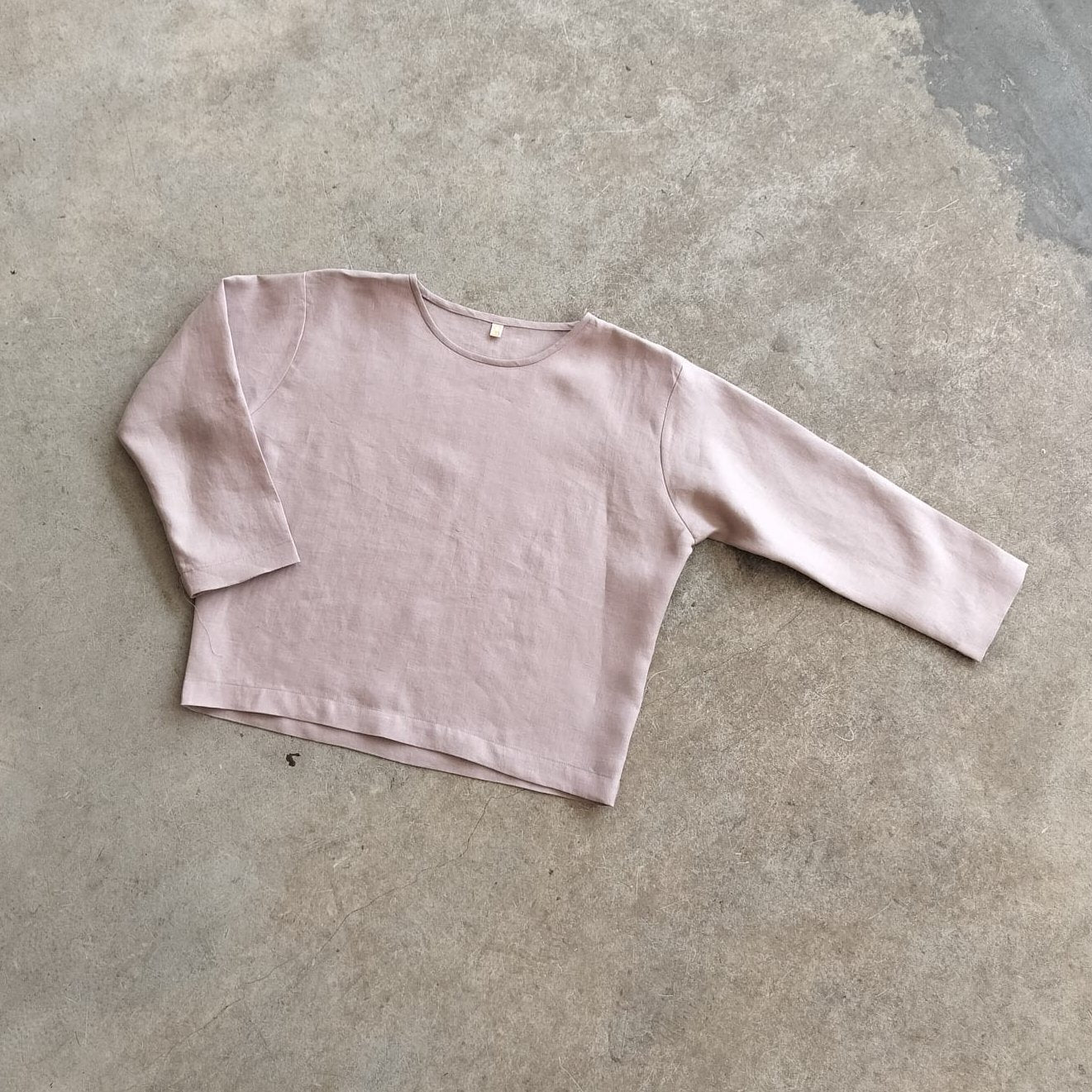 A pink, long-sleeved crop top laid flat on a concrete surface.