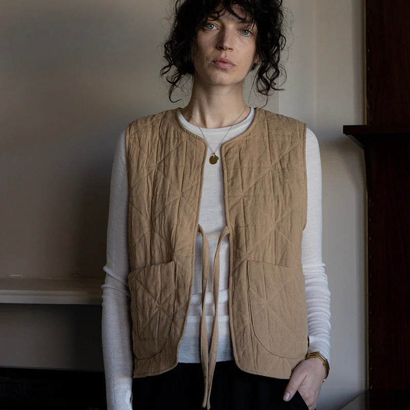 A person wearing a blue gilet with a round neckline and long sleeves, paired with tan trousers.