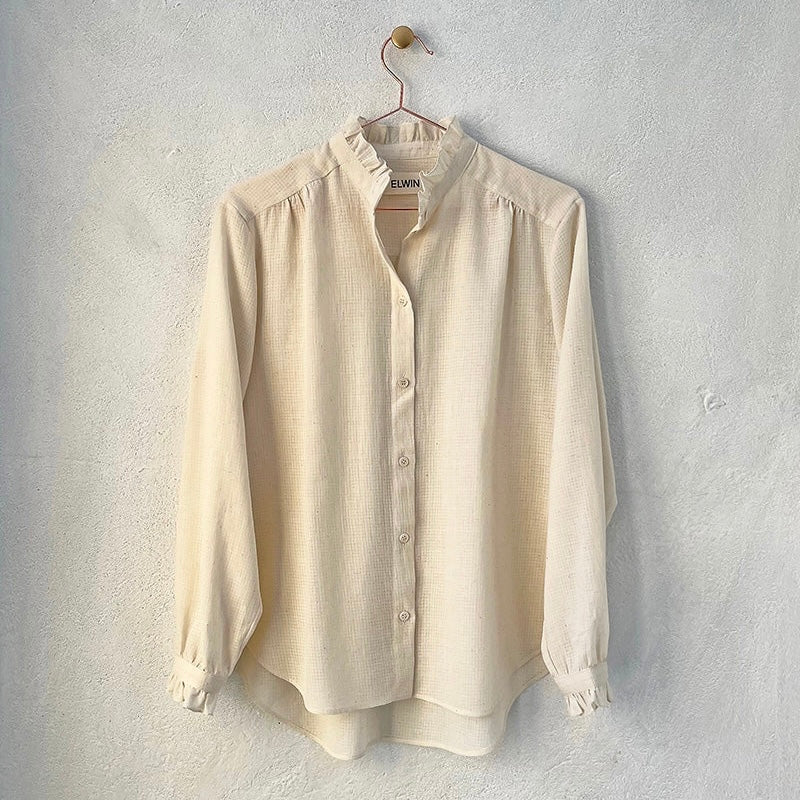 A beige, frill-shirt with a relaxed fit, displayed on a hanger against a neutral background.