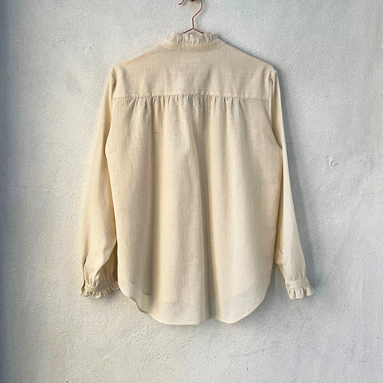 A beige, frill-shirt with a relaxed fit, displayed on a hanger against a neutral background.