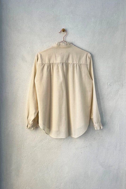 A beige, frill-shirt with a relaxed fit, displayed on a hanger against a neutral background.