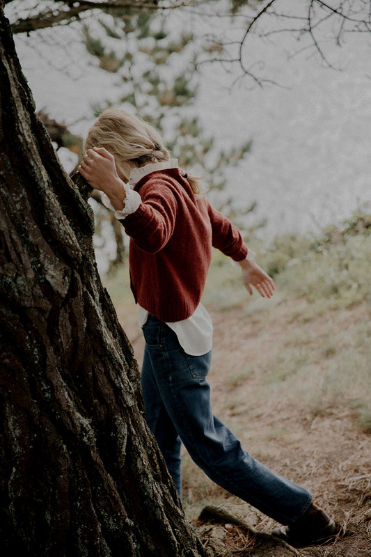 Person in a red sweater and blue jeans standing next to a tree in a natural setting