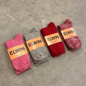 Wool and nylon mix knitted thick socks in pink, taupe, red and multicoloured with folded in half with yellow labels on a grey concrete background