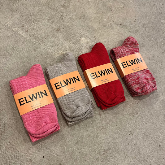 Wool and nylon mix knitted thick socks in pink, taupe, red and multicoloured with folded in half with yellow labels on a grey concrete background
