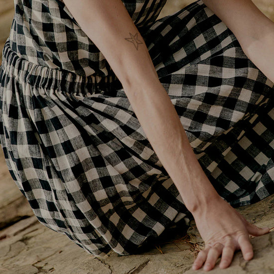 Person wearing a black and white checkered dress sitting on a stone surface.