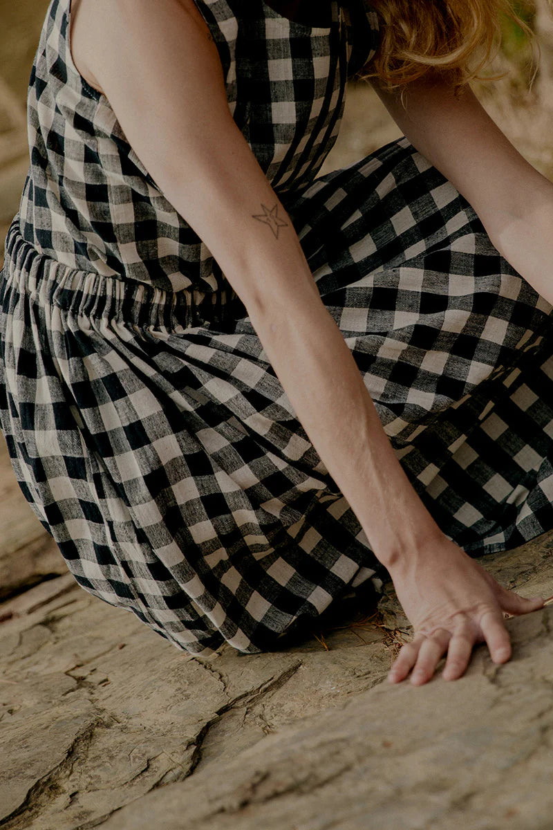 Person wearing a black and white checkered dress sitting on a stone surface.