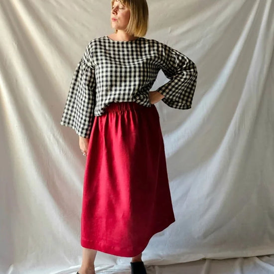 Person wearing a checkered black and white top and red skirt against a plain background