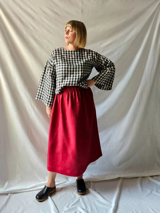 Person wearing a checkered black and white top and red skirt against a plain background