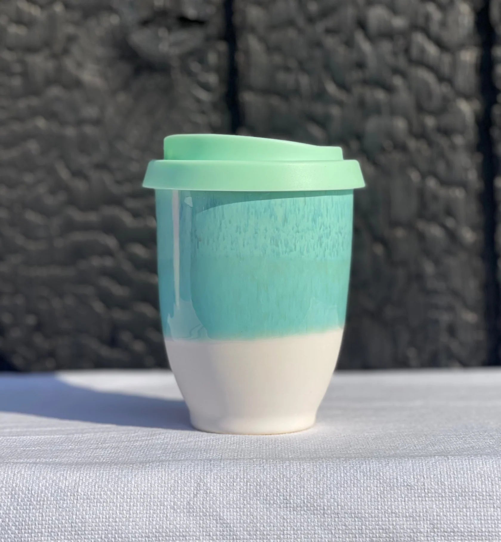 Turquoise and white ceramic cup with a green lid on a textured surface