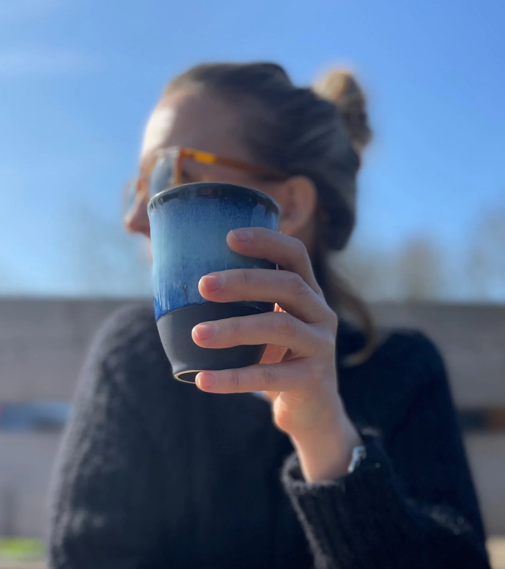 Person holding a blue cup outdoors with a blurred background