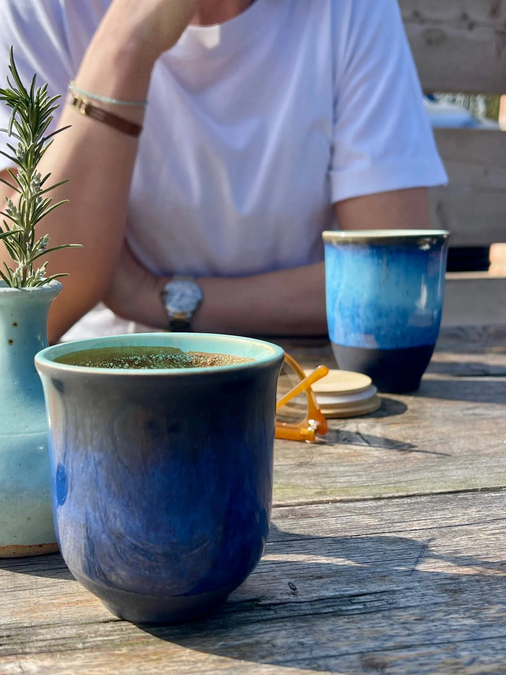 Blue ceramic mug on a wooden table with a person sitting in the background