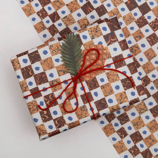 Gift wrapped in patterned paper with red string and a green leaf on a white background