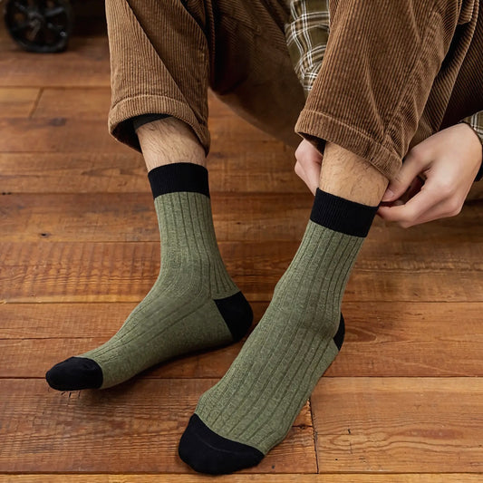 Person wearing green socks with black toes and cuffs on a wooden floor with brown cord trousers