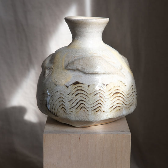 Ceramic vase with wavy patterns and fish on a wooden pedestal against a neutral background