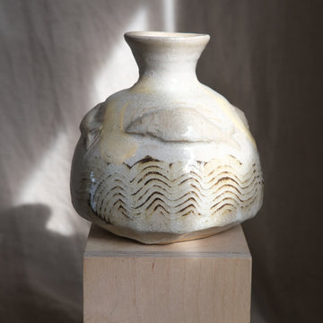 Ceramic vase with wavy patterns and fish on a wooden pedestal against a neutral background