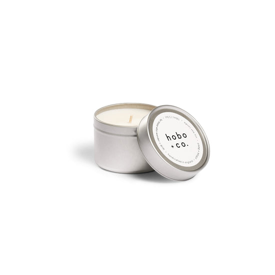 Candle in a metallic tin with 'hobo + co.' label on a white background
