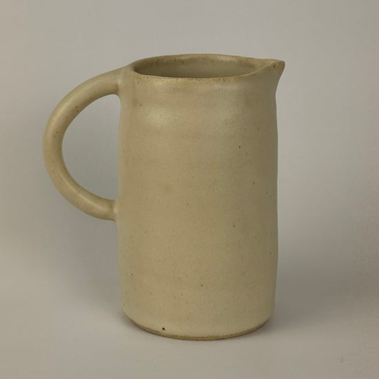 Beige ceramic pitcher on a plain background