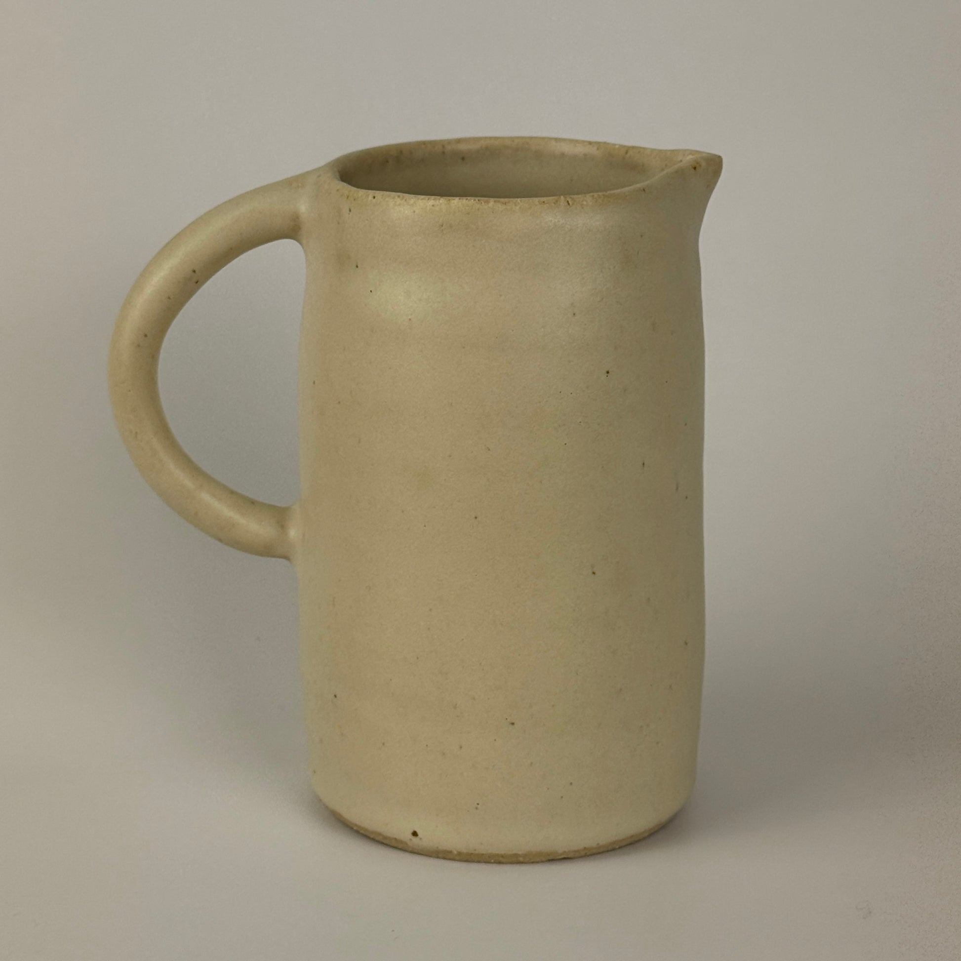 Beige ceramic pitcher on a plain background