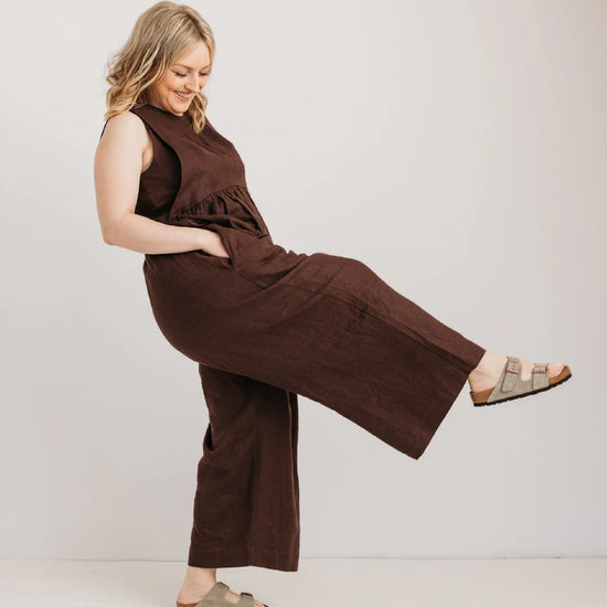 Woman wearing a brown jumpsuit posing against a plain background