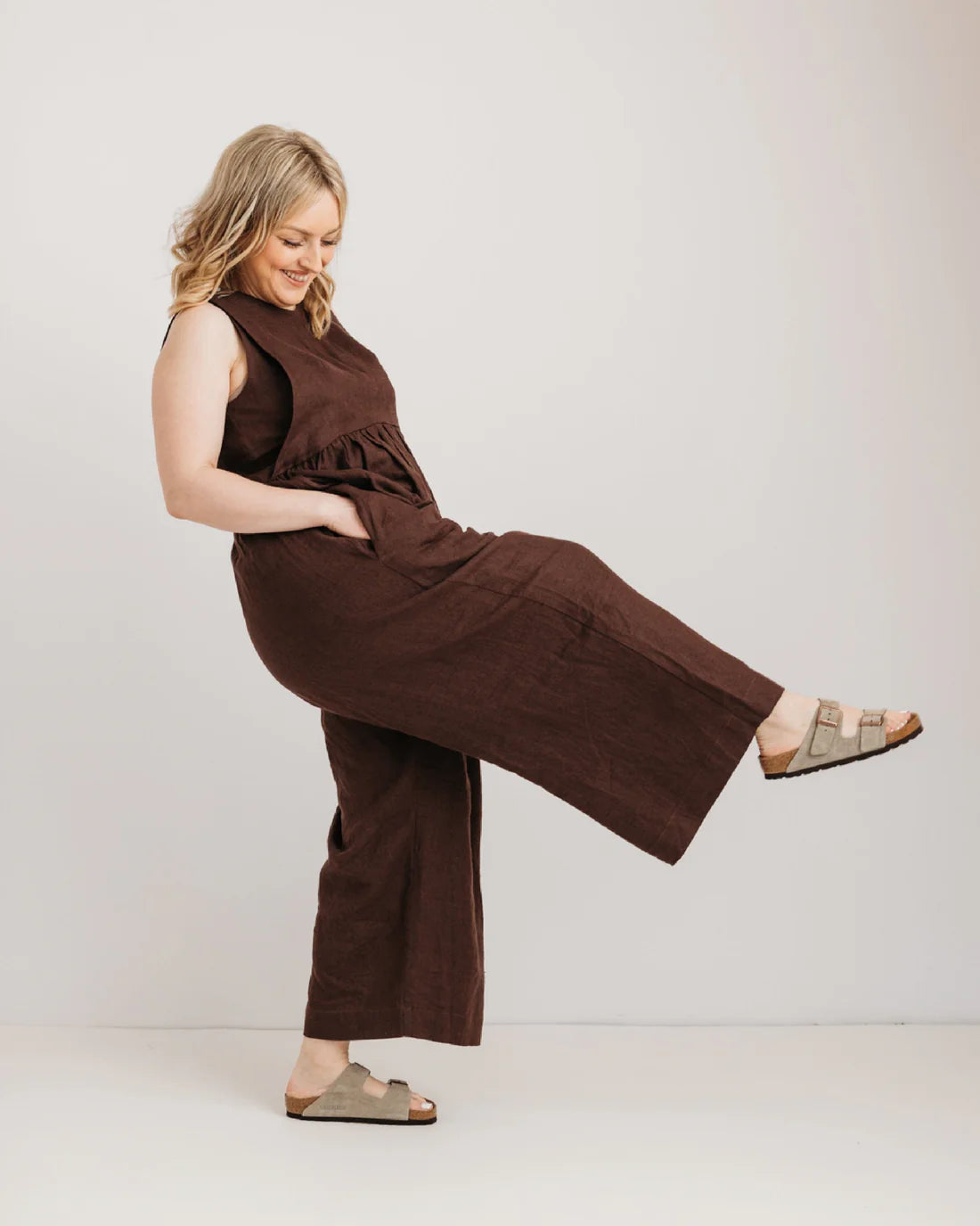 Woman wearing a brown jumpsuit posing against a plain background