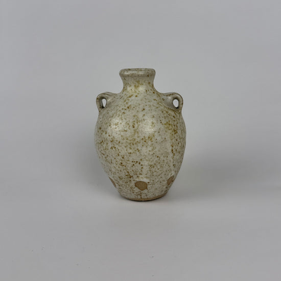 Small ceramic vase with speckled glaze on a gray background