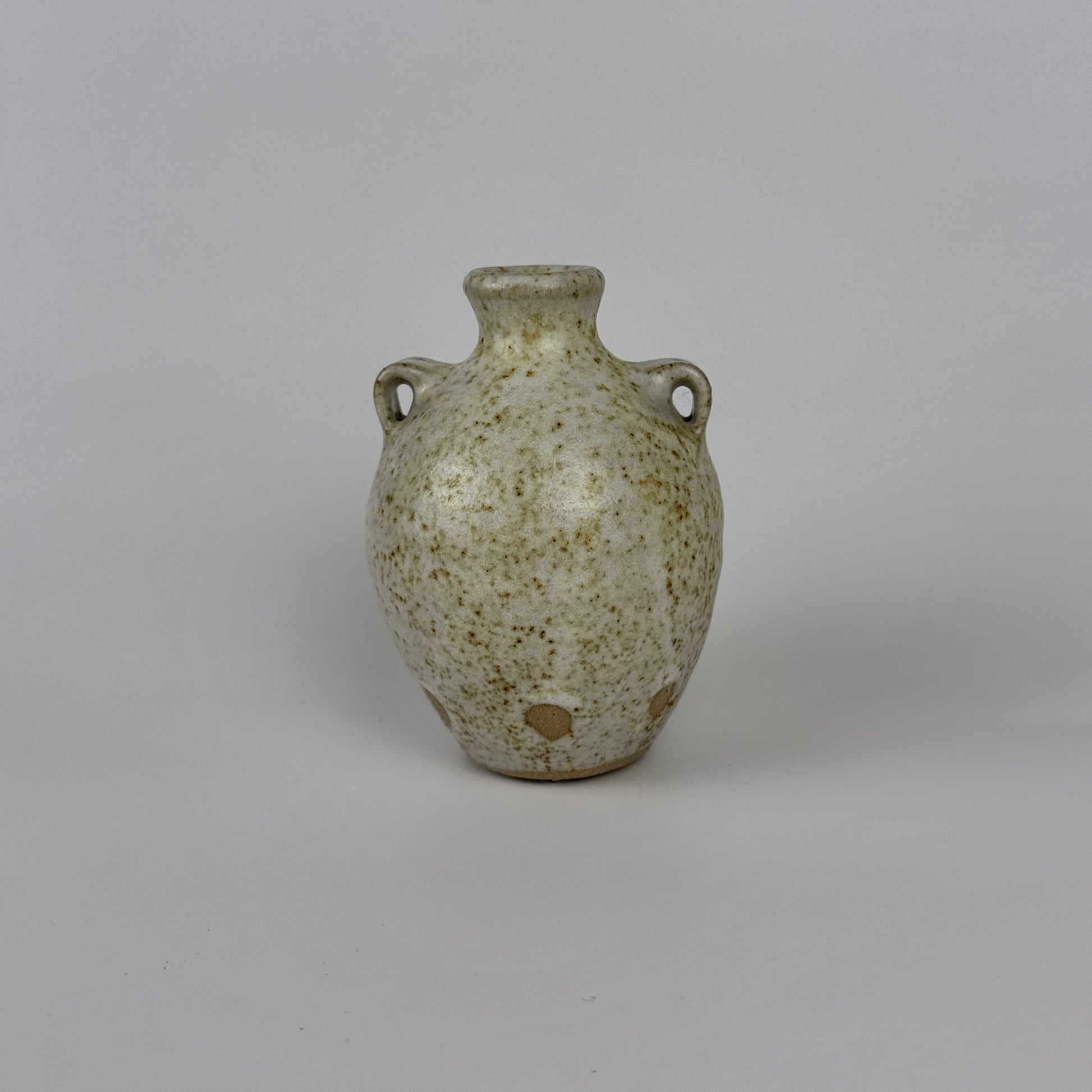Small ceramic vase with speckled glaze on a gray background