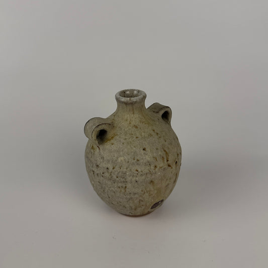 Small ceramic bud  vase with two small holes on a plain background