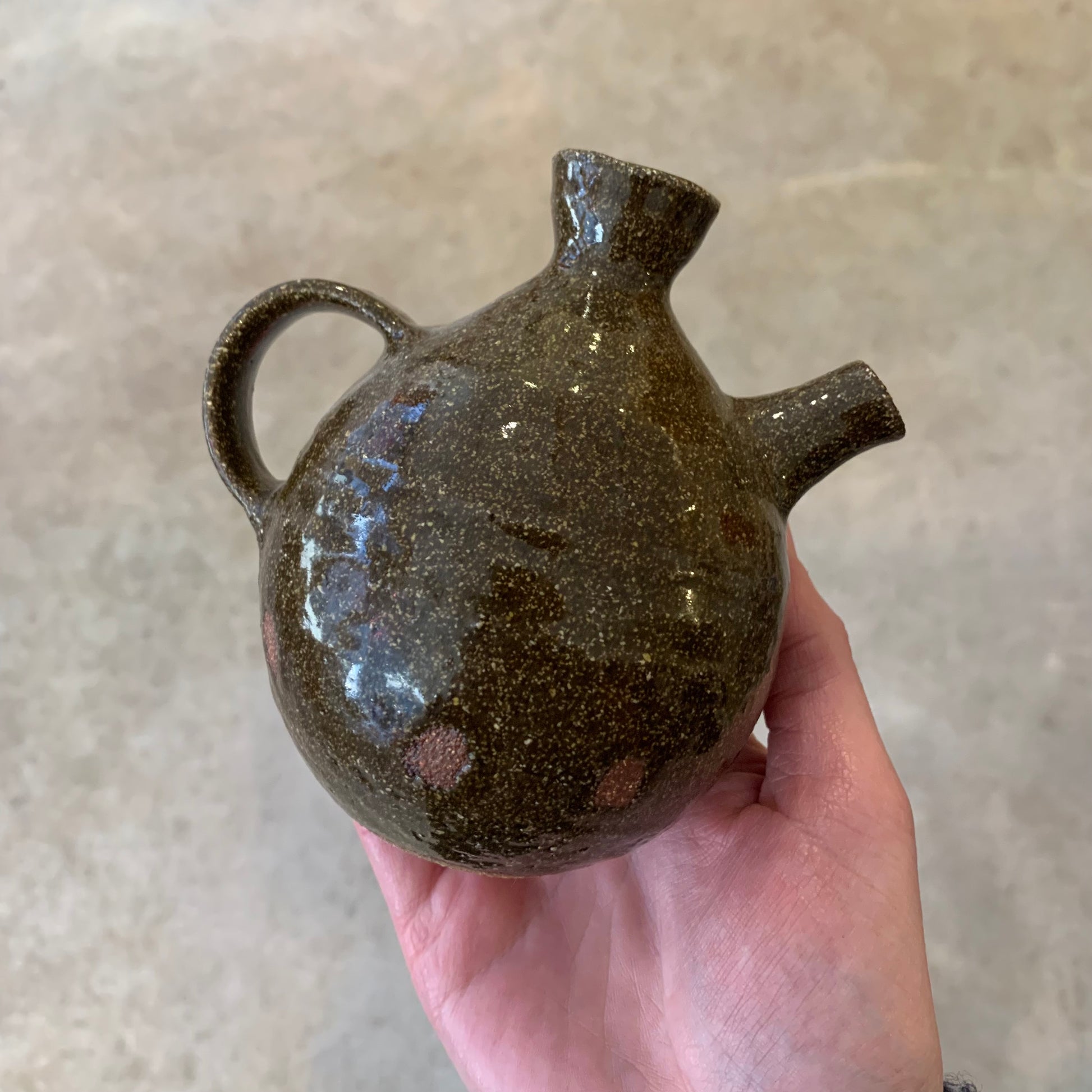 Hand holding a hand thrown cerqamic brown glazed oil pourer