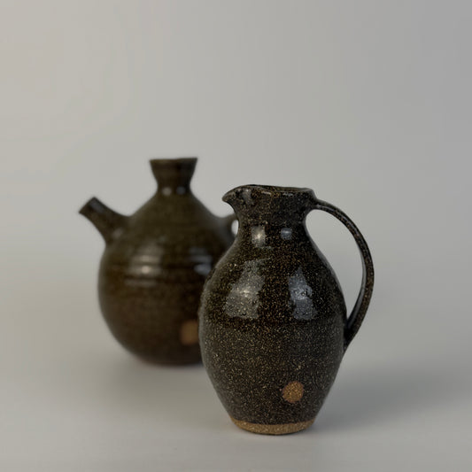 Two dark brown ceramic pitchers on a light gray background