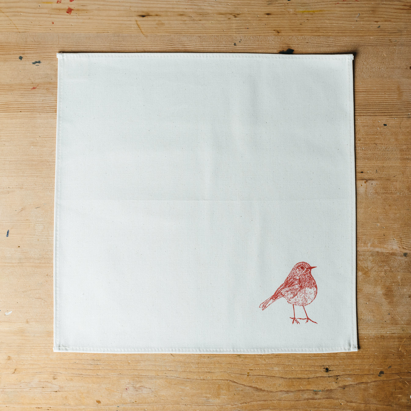 A white napkin on a brown wooden background with a robin printed on the corner