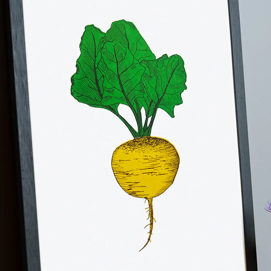 Framed artwork of a yellow root vegetable with green leaves on a white background