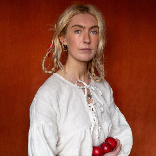 Woman in a white blouse holding red apples against an orange background