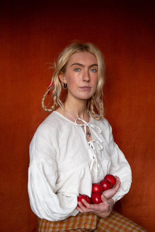 Woman in a white blouse holding red apples against an orange background