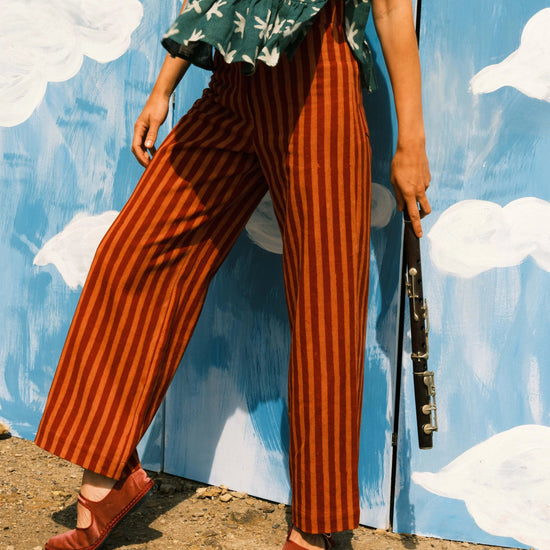 Person wearing a green floral top and red striped pants against a blue wall with white clouds.