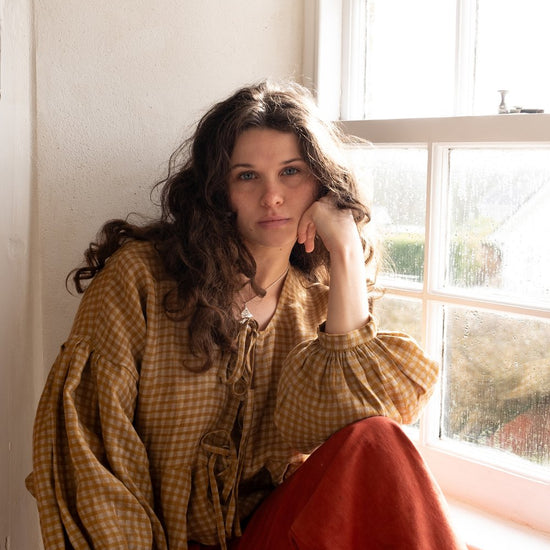 woman wearing flaxen linen top and red trousers sitting on window sill