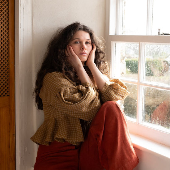 woman wearing flaxen linen top sitting on window sill
