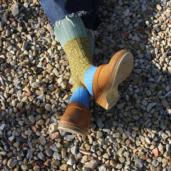 Person wearing brown shoes and multicolored socks on a gravel surface