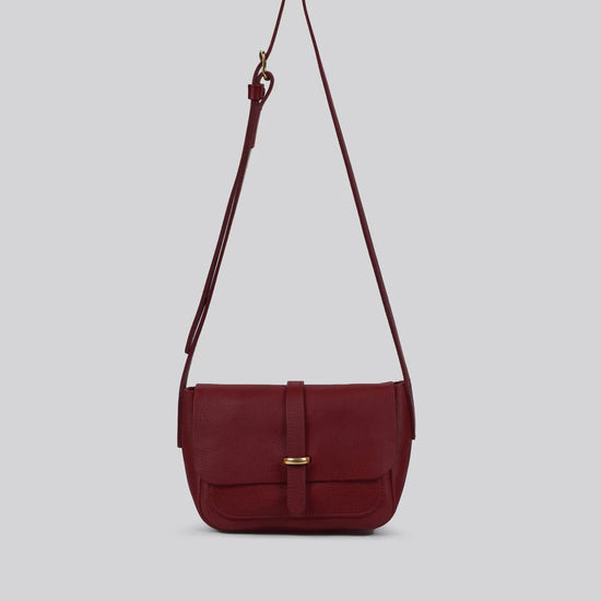 Maroon Red shoulder bag with a strap and brass details on a light gray background