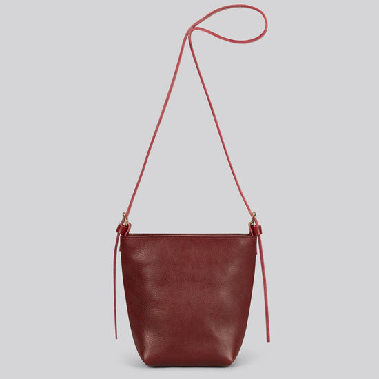 Maroon red leather shoulder bag with a strap on a light gray background