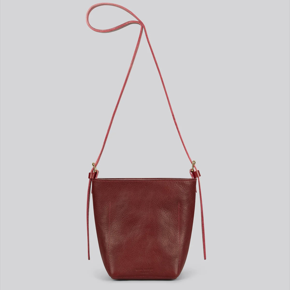 Handmade luxury maroon leather handbag with a strap on a light gray background