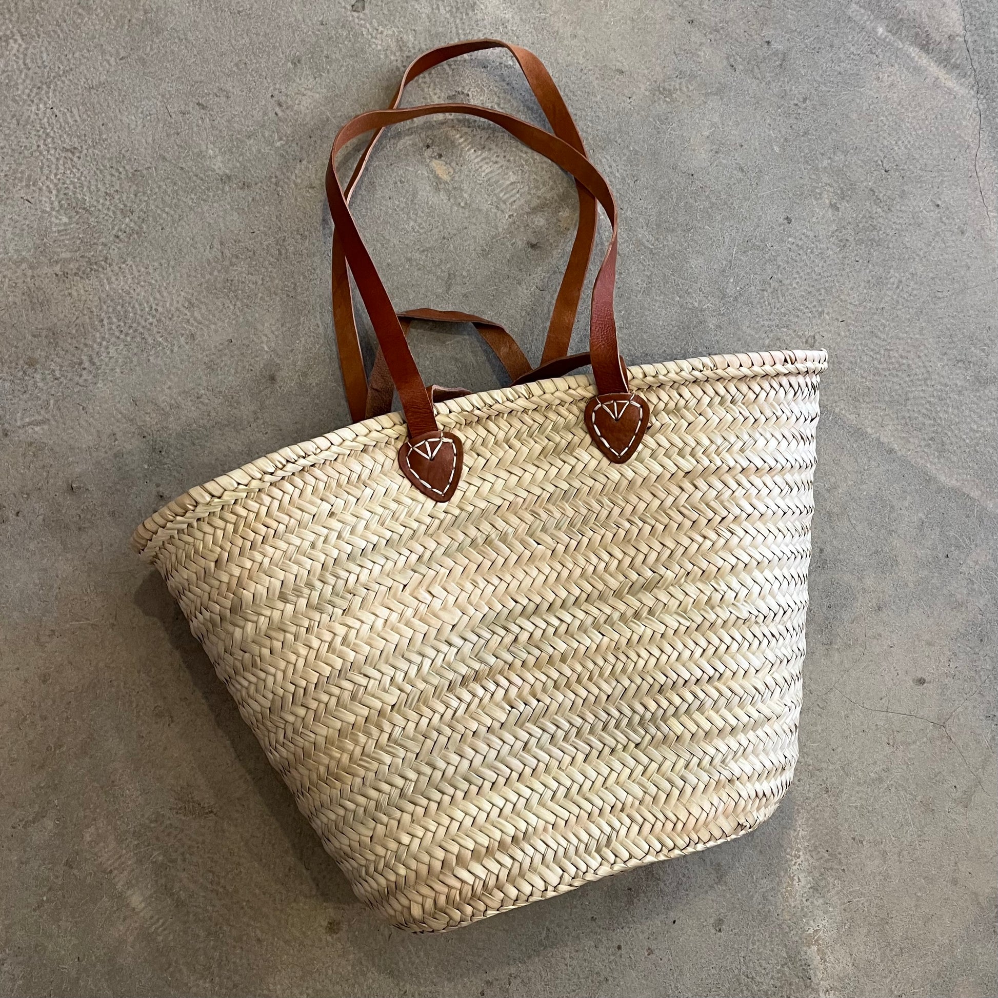 woven palm market bag with leather straps on a concrete background