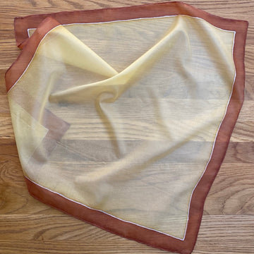 Beige square scarf with brown border on a wooden surface