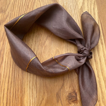 Brown silk scarf with gold trim on a wooden surface